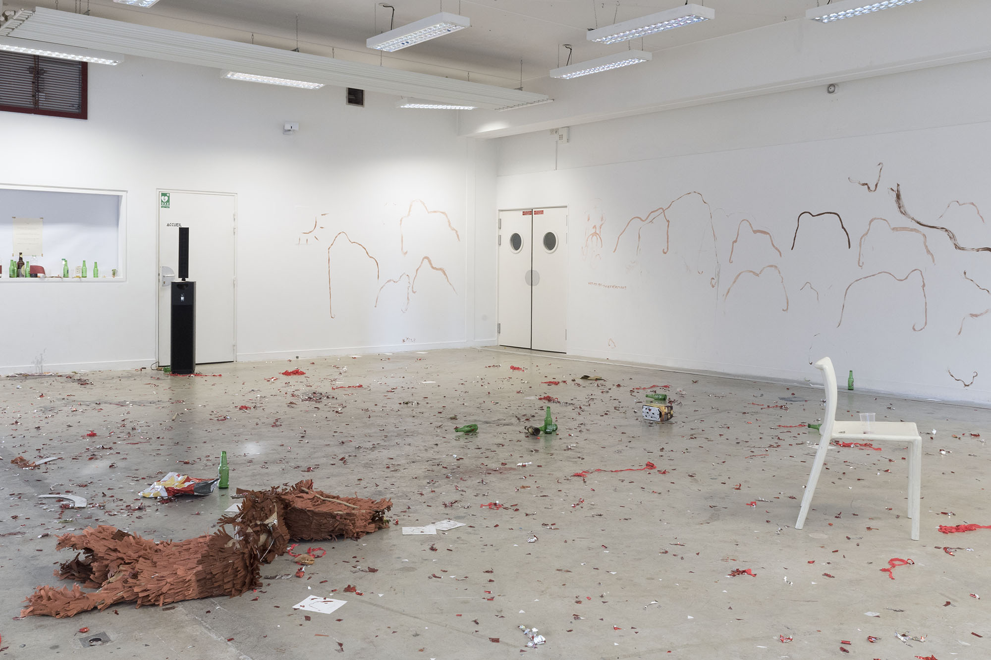 photo du lendemain : les murs sont recouerts de dessins de mammouth mais il y a aussi un soleil. le piñata est en morceaux par terre, les cotillons sont partout, des bouteilles de bières jonchent le sol, une chaise est au milieu de tout ça.